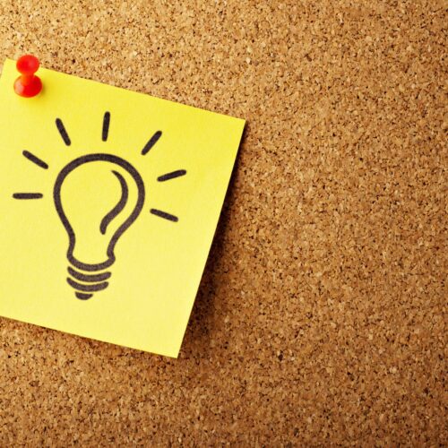absolutvision-82TpEld0_e4-unsplash Korkpinnwand als Hintergrund mit einem angepinnten gelben Post-it-Zettel, auf dem eine leuchtende Glühbirne gezeichnet ist